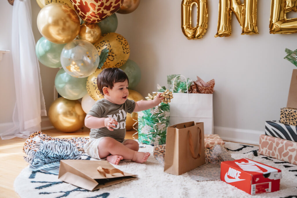 Luca is One! Wild One First Birthday Party - All the details of Luca's Wild One Safari Themed First Birthday. Wild One balloon backdrop and wild one tee. Safari balloon garland. Animal print gift wrap. Sitting on alphabet rug.