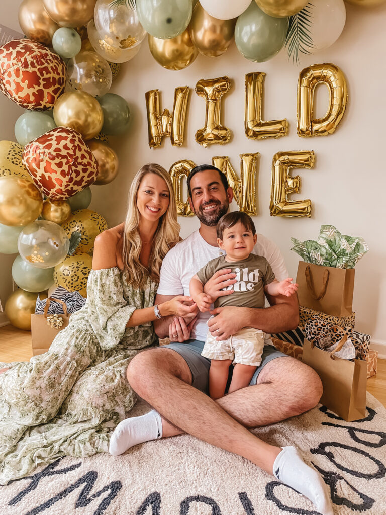 Luca is One! Wild One First Birthday Party - All the details of Luca's Wild One Safari Themed First Birthday. Wild One balloon backdrop and wild one tee. Safari balloon garland. Sitting on alphabet rug.