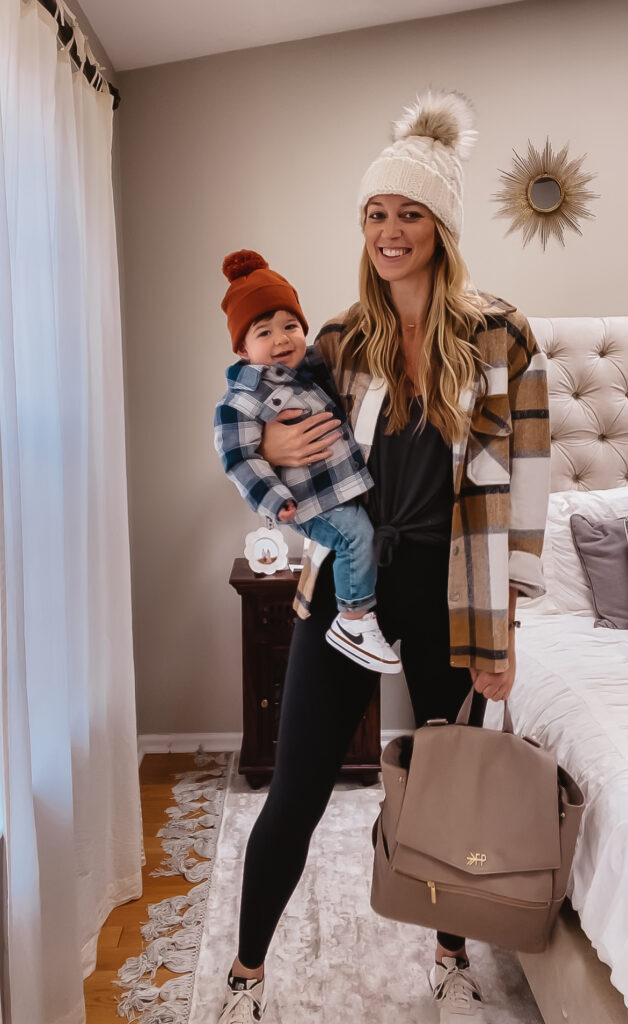 Fall Outfit Inspo: 7 Coordinating Mommy & Me Styles. Toddler boy fall outfit. Plaid quilted toddler jacket, toddler skinny jeans, toddler thermal hoodie, toddler Nike sneakers & knit pom beanie for babies and toddlers. Women's oversized v-neck comfy tee, basic black leggings, neutral plaid shacket, chic leather diaper bag backpack & black and white new balance sneakers.