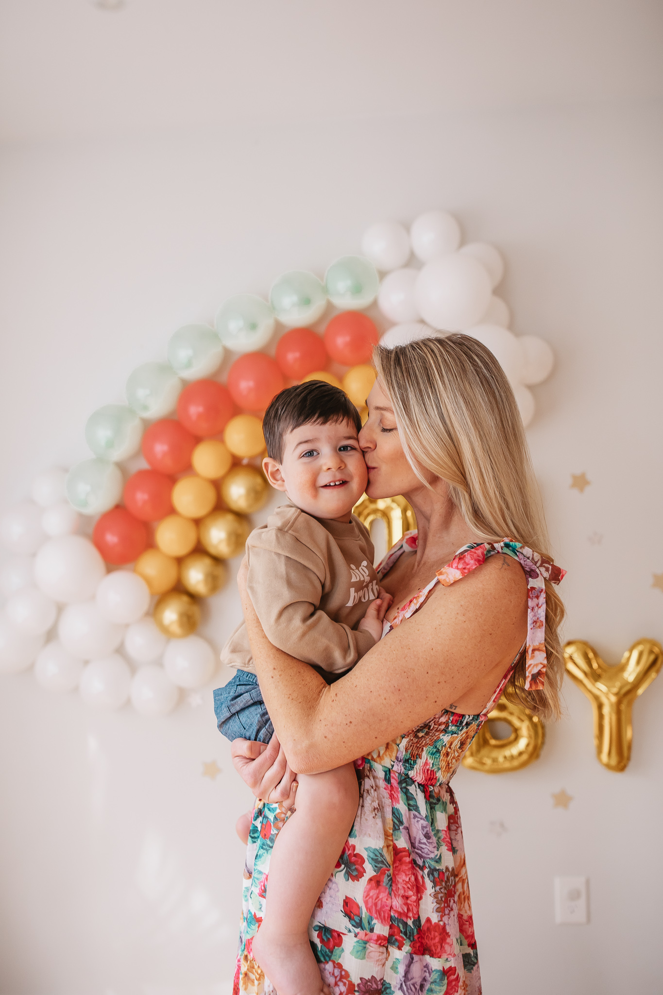 DIY Rainbow Baby Pregnancy Announcement. Mommy to be and big brother in front of rainbow baby balloon backdrop for photos.