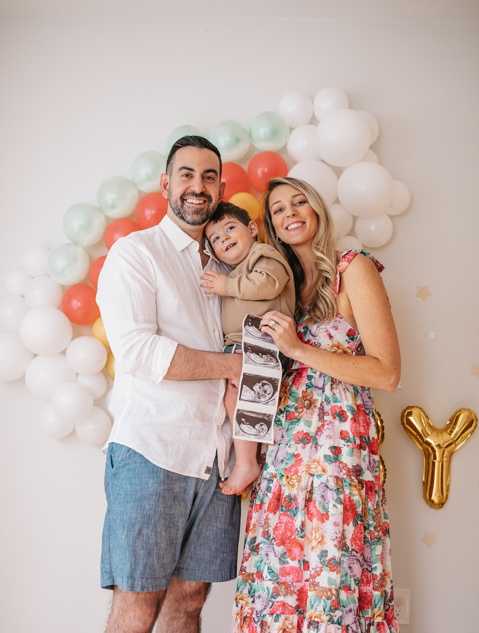 DIY Rainbow Baby Pregnancy Announcement. Family photos in front of rainbow baby balloon backdrop for with ultrasound.